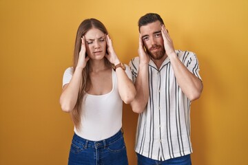 Young couple standing over yellow background with hand on head, headache because stress. suffering migraine.