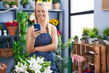 Young blonde woman florist smiling confident using smartphone at florist store