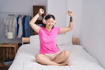 Chinese woman listening to music sitting on bed at bedroom