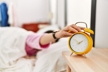 Girl turning off alarm clock lying on the bed at bedroom.