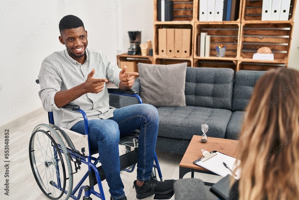 Poster african american man doing therapy sitting on wheelchair pointing fingers to camera with happy and f