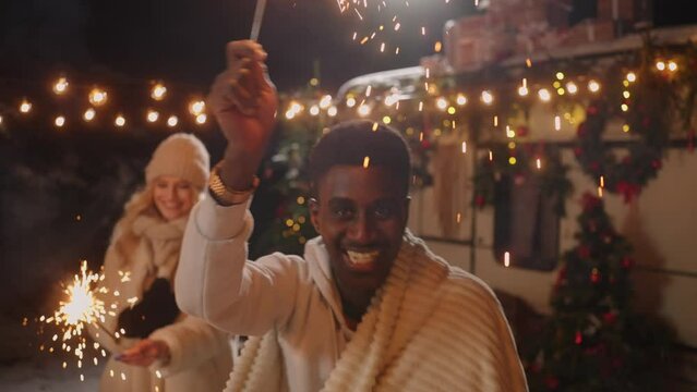 joyful african american man is swaying sparkler and smiling cheerfully to camera, merry Xmas party