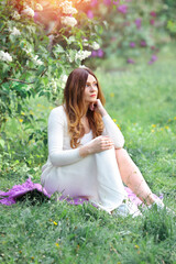 Naklejka na ściany i meble A beautiful girl in a white dress is sitting in a spring garden. Rest at nature. Relax concept