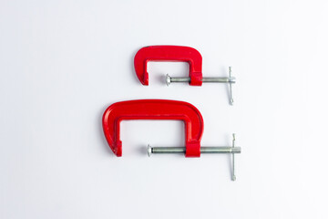 Two red metal clamps of different sizes on a white background. Tools for repair work and DIY projects. Construction, craft, work with wood products.