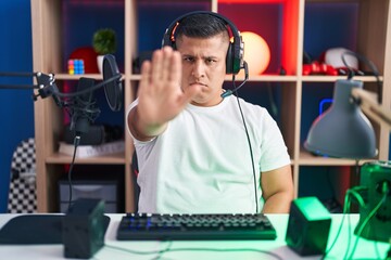 Young hispanic man playing video games doing stop sing with palm of the hand. warning expression with negative and serious gesture on the face.