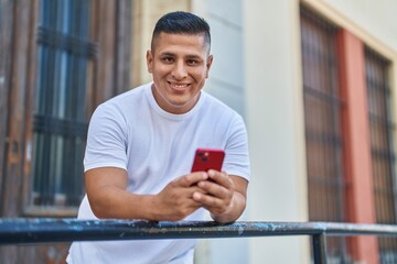 Young latin man using smartphone leaning on balustrade at street