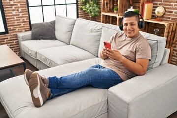 Young latin man listening to music sitting on sofa at home