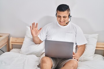 Hispanic young man using computer laptop on the bed looking positive and happy standing and smiling with a confident smile showing teeth