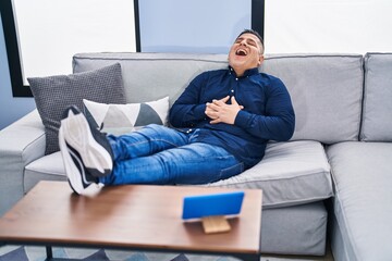 Fototapeta premium Young latin man watching movie on touchpad sitting on sofa at home
