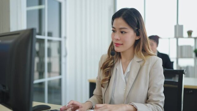 Smilling face of asian woman customer support agent or call center wearing headphone and works on desktop computer and crossed arms at office