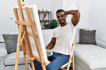Young african man painting on canvas at home smiling confident touching hair with hand up gesture,...