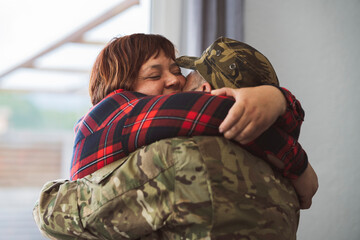 Hispanic veteran soldier hugging his wife when returning from military service to home. Love and family concept. Focus on latin mature woman face - obrazy, fototapety, plakaty