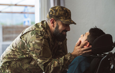 Hispanic veteran soldier caresses disabled son in a wheelchair when returning from military service to home . Unconditional love and inclusion concept. Focus on father face
