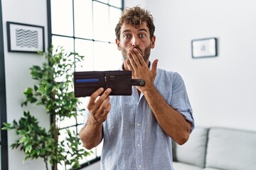 Young handsome man holding leather wallet covering mouth with hand, shocked and afraid for mistake....