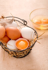Different eggs in metallic basket on beige background. Raw broken eggs in glass bowl.