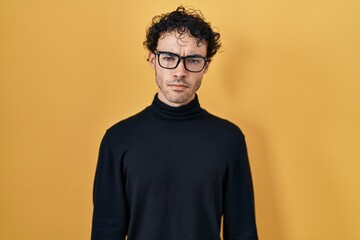 Fototapeta premium Hispanic man standing over yellow background skeptic and nervous, frowning upset because of problem. negative person.