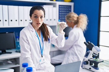 Young hispanic woman working at scientist laboratory scared and amazed with open mouth for surprise, disbelief face