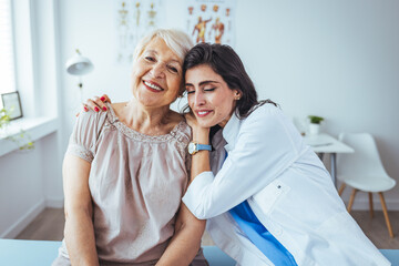 Fototapeta premium Young care specialist is sitting beside granny and hugging her. Old woman is bit scared and lonely so she is getting needed comforting. Caring young medical doctor hugging patient.