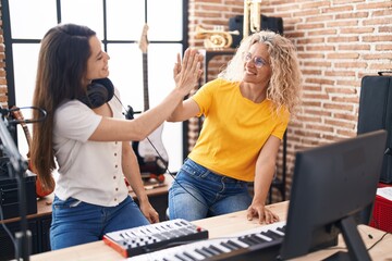 Two women musicians high five with hands raised up at music studio