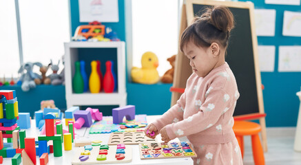Adorable chinese girl playing with maths puzzle game standing at kindergarten