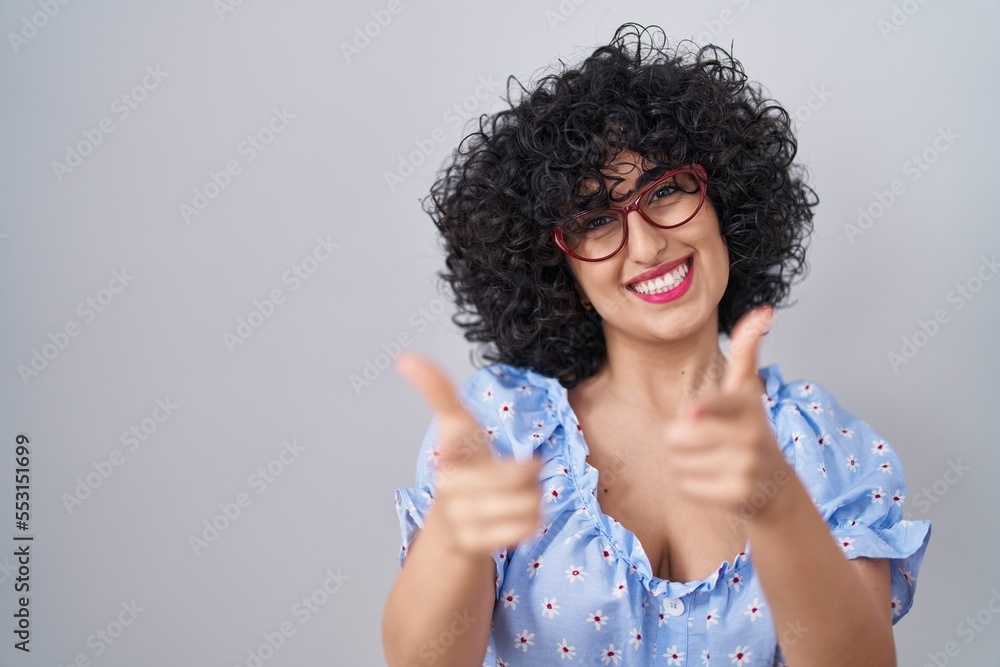 Sticker young brunette woman with curly hair wearing glasses over isolated background pointing fingers to ca