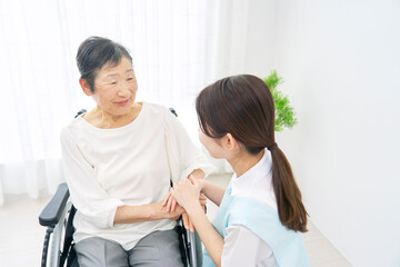 車椅子に乗る高齢者女性と会話する介護士