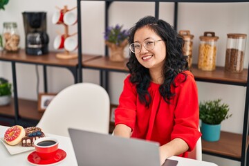 Young chinese woman having breakfast using laptop at home