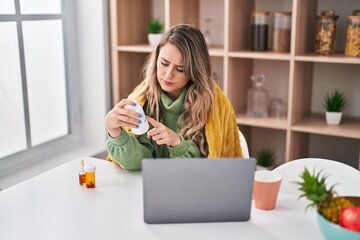 Fototapeta premium Young woman holding pills having telemedicine at home