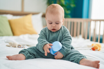 Adorable caucasian baby holding toy sitting on bed at bedroom