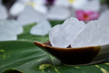 Soft focus of Alum cubes on small ceramic cup, blurred  plumeria flowers background, concept for herb, bodycare, skincare, waterclear, spa, treatment, disease protection and protect armpit smell.