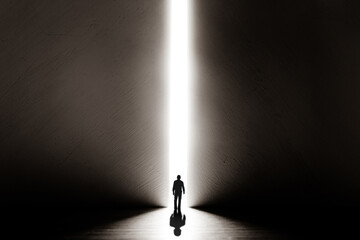 The silhouette of a man walking towards a bright light in the opened huge wall. A light in the end of a tunnel. The concept of success, freedom of choice, open mind, meditation. - 553152687