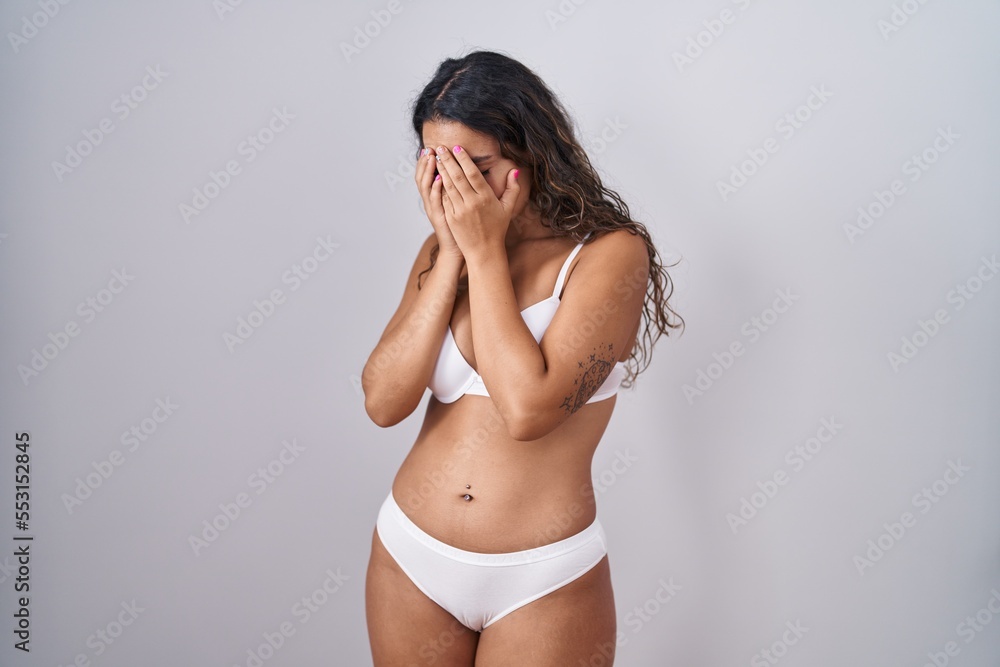 Sticker young hispanic woman wearing white lingerie with sad expression covering face with hands while cryin