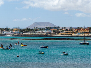 Fototapeta na wymiar Corralejo bay with boats, surf school and houses and mountains in the background, Spain