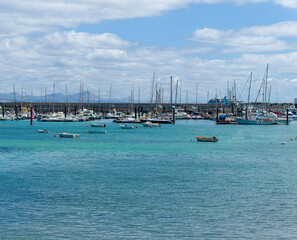 Obraz premium The bay and part of the port of Corralejo with boats, surf school, houses and mountains in the background, Spain