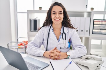 Young hispanic woman wearing doctor uniform smiling confident at clinic