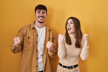 Fototapeta na wymiar Young hispanic couple standing over yellow background celebrating surprised and amazed for success with arms raised and eyes closed. winner concept.