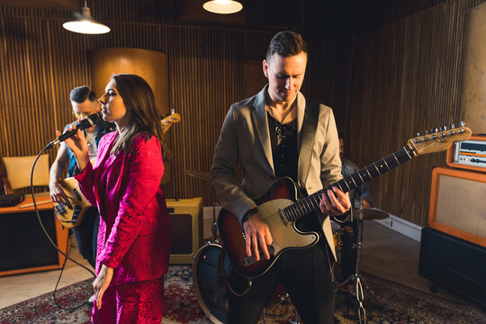 Musicians in recording studio. Process of creating a music album. Group members - mid adult male guitarist and fashionable female singer - in the foreground. High quality photo - Powered by Adobe