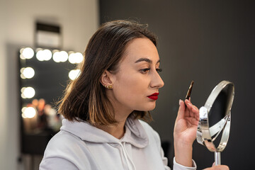 close-up of a woman paints her eyebrow with paint with a bone to a small make-up mirror.
