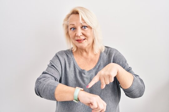 Middle age caucasian woman standing over white background in hurry pointing to watch time, impatience, upset and angry for deadline delay