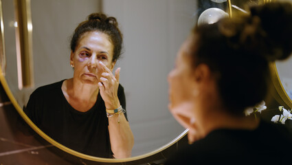 Middle age hispanic woman using makeup to cover signs of domestic violence at bathroom