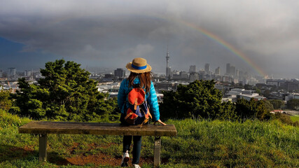Backview of young tourist woman looking view with rainbow in the sky at Auckland city skyline at...