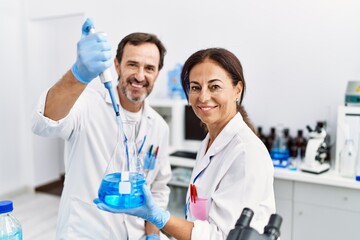 Middle age man and woman partners wearing scientist uniform using pipette and test tube at laboratory