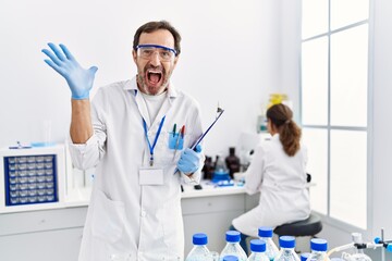 Middle age man working at scientist laboratory celebrating victory with happy smile and winner expression with raised hands