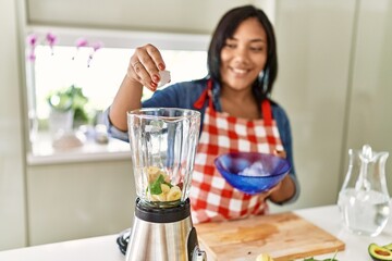 Hispanic brunette woman preparing fruit smoothie with ice at the kitchen