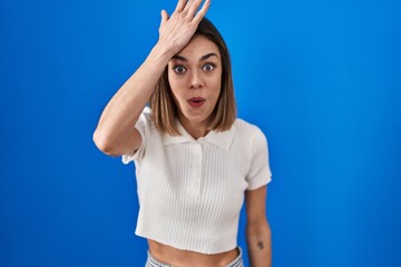 Fototapeta na wymiar Hispanic woman standing over blue background surprised with hand on head for mistake, remember error. forgot, bad memory concept.