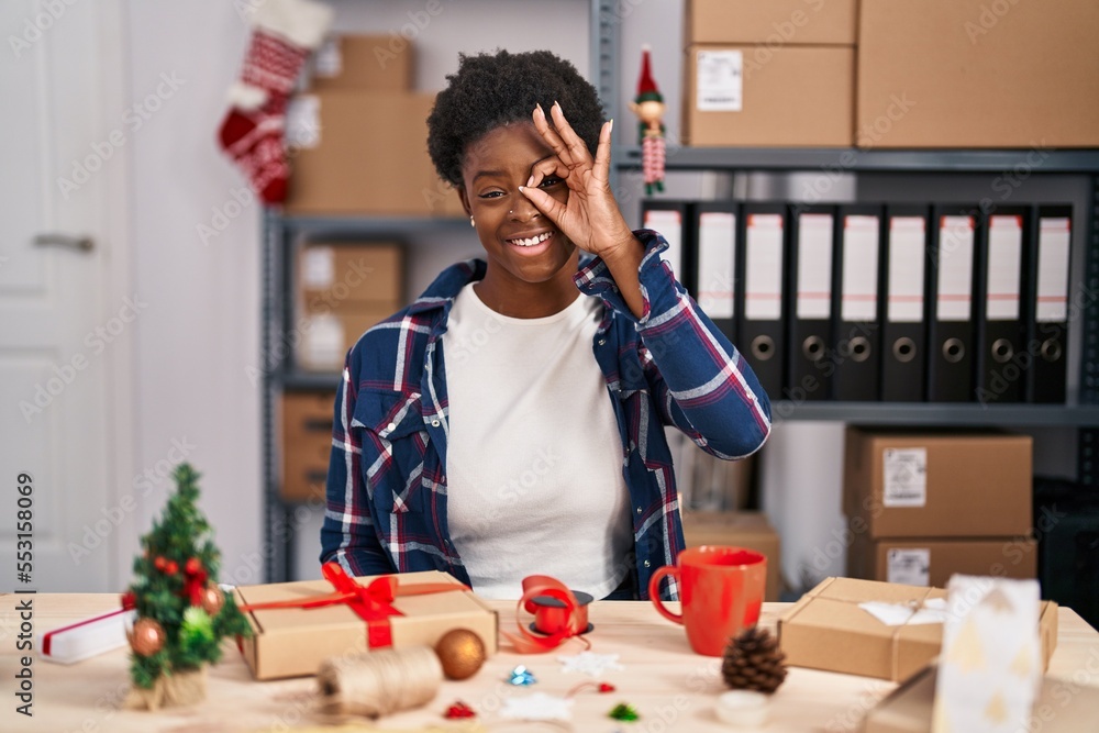 Canvas Prints African american woman working at small business doing christmas decoration doing ok gesture with hand smiling, eye looking through fingers with happy face.