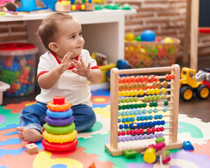 Adorable hispanic baby playing with abacus and hoops game applauding at kindergarten