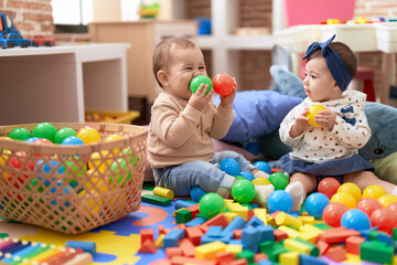 Two toddlers playing with balls sitting on floor at kindergarten