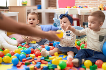 Fototapeta premium Group of toddlers playing with toys sitting on floor at kindergarten