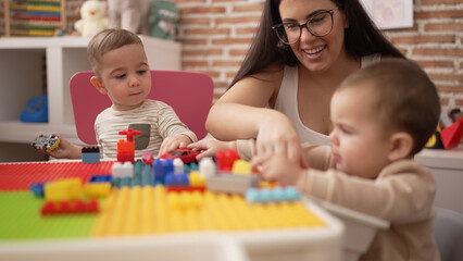 Obraz na płótnie Canvas Teacher and preschool students playing with construction blocks sitting on table at kindergarten